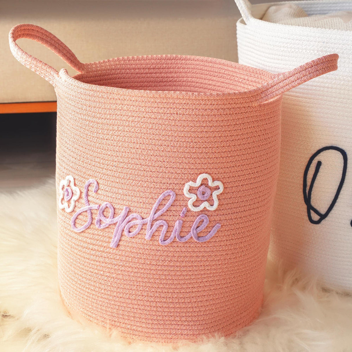 a pink basket with a name on it next to a white basket with a flower