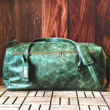 a green leather duffel bag sitting on top of a wooden floor