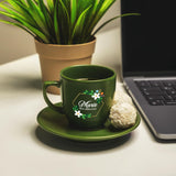 a green coffee cup sitting on a saucer next to a laptop