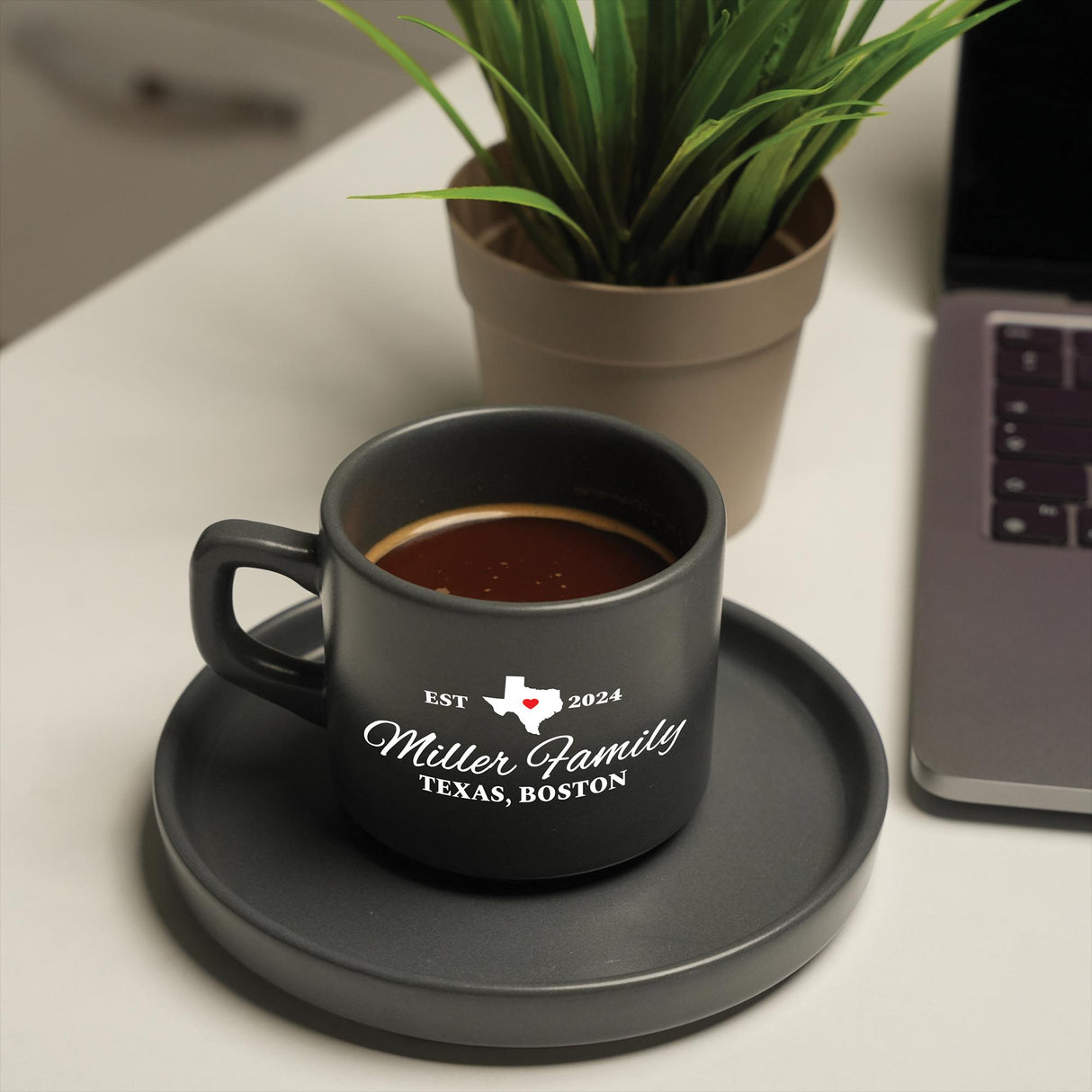 a cup of coffee on a saucer next to a laptop