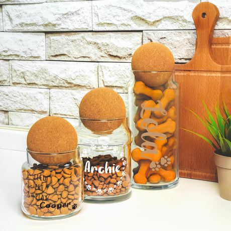 three glass jars filled with dog treats next to a plant